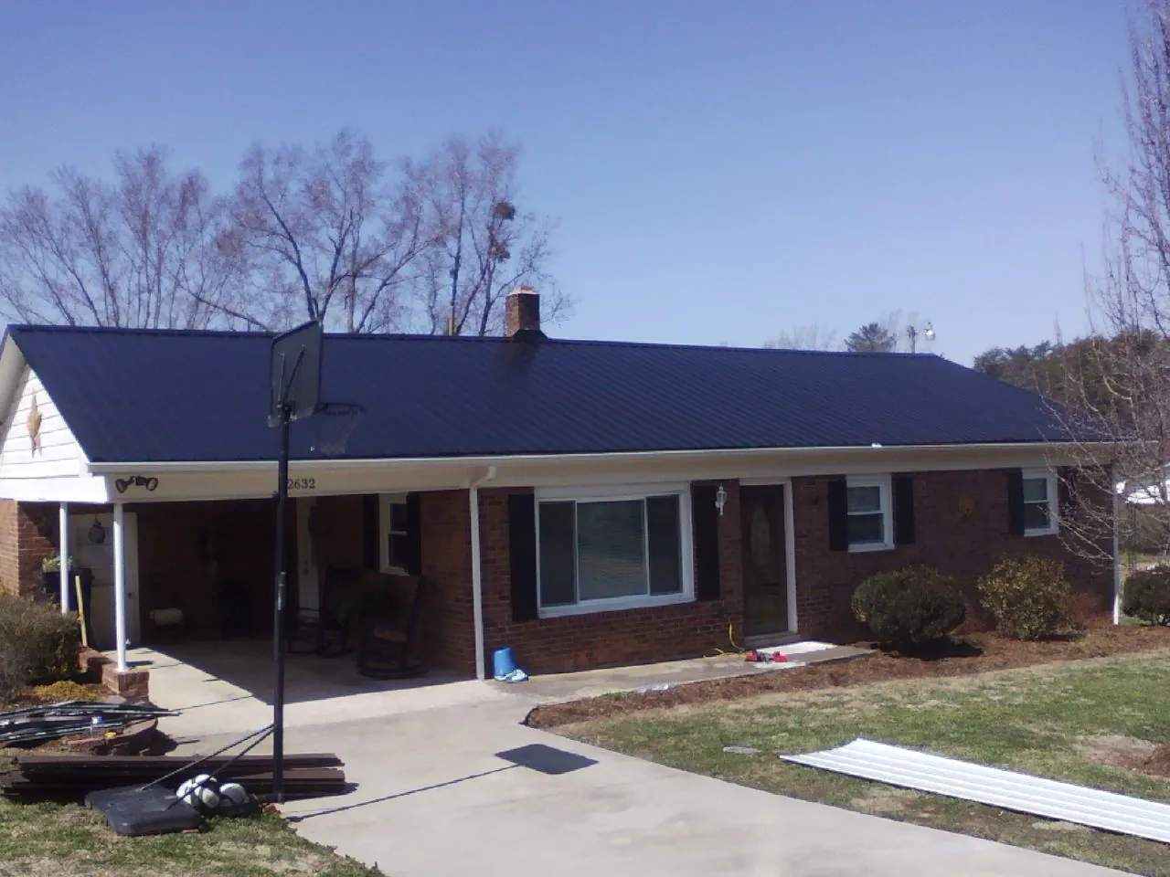 Finished dark blue metal roof on a brick ranch with a carport in Beaver